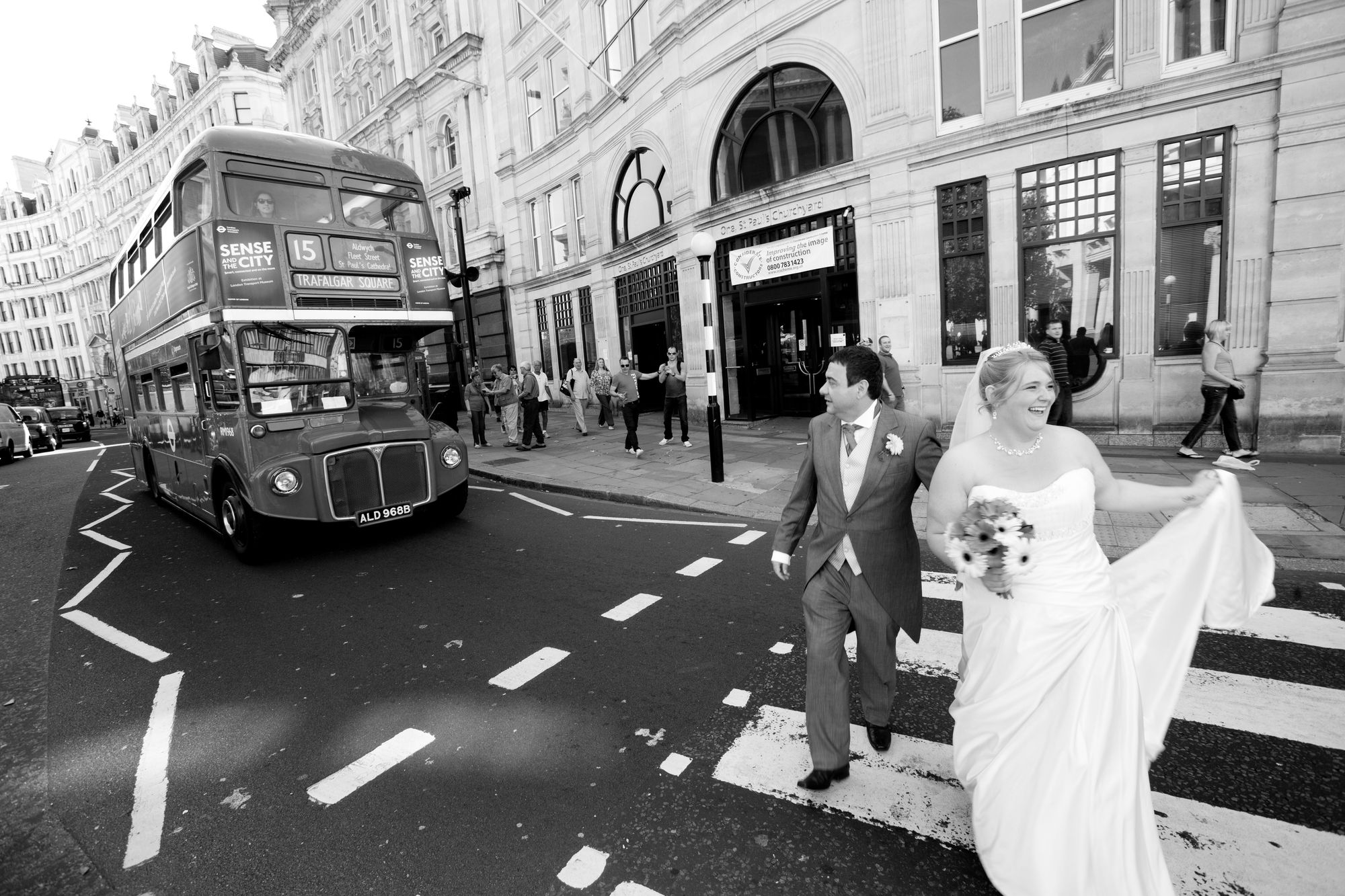 Wedding couple crossing a street in London with a red double-decker bus